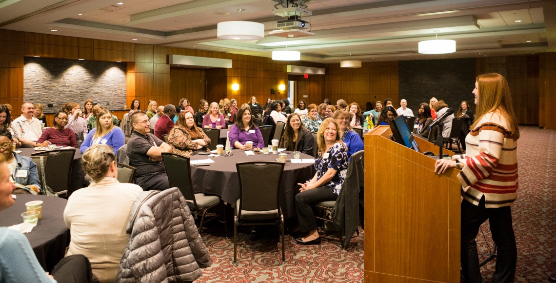 Staff gather in a large room to eat breakfast and listen to a speaker