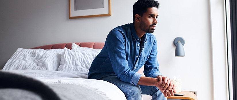 Young man thoughtfully resting on the edge of a bed