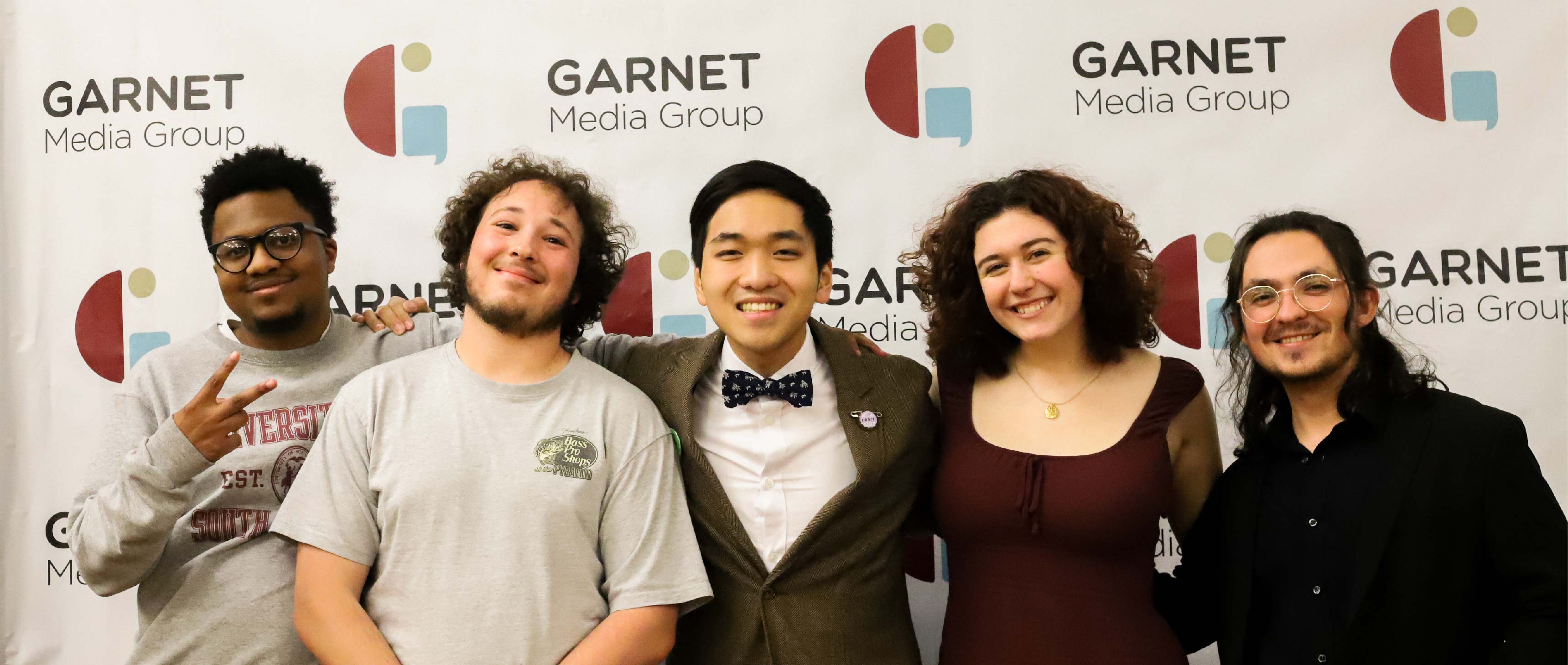 A group of five diverse individuals, smiling and standing close together in front of a Garnet Media Group banner.