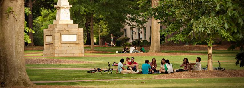 About 10 students sit in a circle on the grass on the Horseshoe, with the Maxcy monument and other students in the background