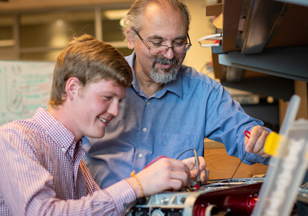 A student works on an a piece of equipment with a professor watching on. 