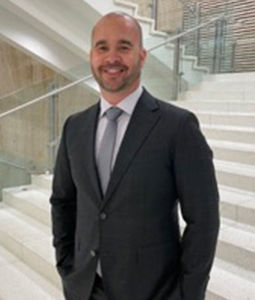 a man in dark gray suit smiling on white marble stairs