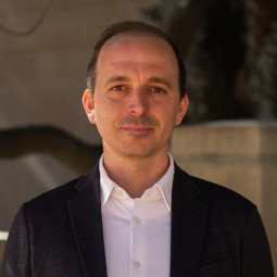 Guillermo wears a white polo under a black blazer and stands facing the camera