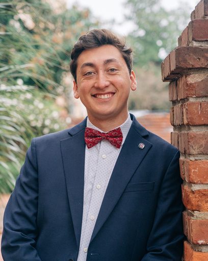 Smiling man with short brown hair in a navy blue suit and a garnet, Gamecock patterned bow tie.