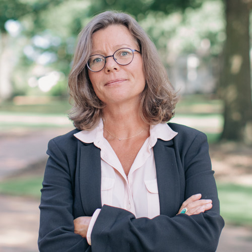 Woman with shoulder length hair and glasses, wearing a white collared shirt with a black blazer