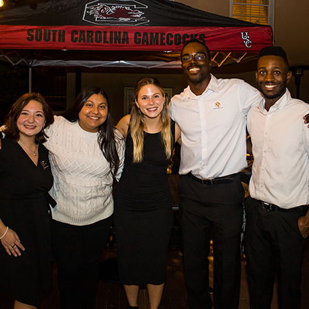 Five people pose for a photo outside of McCutchen House on the evening of the HRSM Homecoming party.