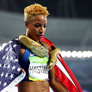 woman with track shoes around her neck and a U.S. flag draped on her shoulders stands in an arena