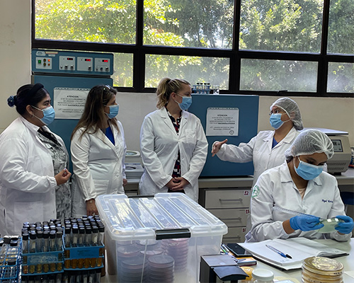 five people stand in a labe wearing white coats and face masks